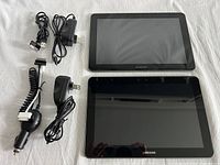 Two Samsung Galaxy tablets with multiple chargers photographed on white fabric background.