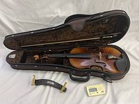 Open hard case showing violin body, bow, shoulder rest and tuner