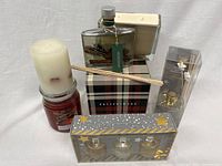 Lot of new and unused candles and diffusers arranged on white background including pillar candle, jar candle, glass container candle, botanical diffuser, reed sticks, and boxed diffuser set