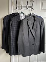 Four men's designer clothing items hanging on wall hooks including two jackets visible in front, one dark solid and one checked pattern suggesting sports jackets from Hugo Boss along with other garments.