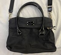 Front view of black nylon handbag with fold flap compartment, double PVC handles, and adjustable removable crossbody strap laid out flat.