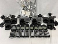 Two sets of Panasonic cordless phones with a total of eight handsets, four charging docks, two base stations, and multiple power adapters arranged on a surface.