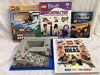 Set of four Lego books displayed alongside a raised Lego base plate with ramp and ditch.