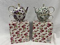 Both mini teapot sets shown on top of their floral patterned boxes, stacked teapot on matching teacup for each set.