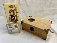 Photo showing vintage style original packaging with illustration of girl and kitten, and rectangular wooden music box with metal crank and decorative metal corners.