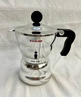 Front and side view of shiny, polished metal 1-cup Moka espresso maker with black handle and knob, displaying AdiALESSI logo and MOKA ALESSI mark.