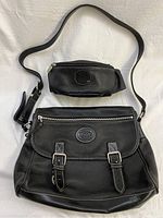 Front view of both Roots black leather handbags, larger flap-style bag with buckle straps and smaller zippered pouch bag, showing overall condition and detailing