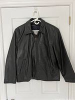 Front view of black genuine leather jacket, zip closure, collar, two vertical zip pockets.