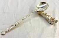 Vintage metal dragon spoon resting on dragon-shaped spoon rest showing detailed dragon design and Greek key pattern on handle