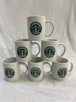 Photo showing all six Starbucks white ceramic mugs stacked in a pyramid shape, displaying the green Starbucks Coffee logo on each.