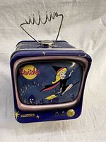 Front view of vintage Bewitched tin coin bank shaped like tube TV showing cartoon witch,broomstick, and Vandor logo.