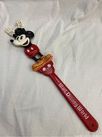 Full view of the vintage Mickey Mouse shoe horn showing the red handle with 'Walt Disney World' text and Mickey figure with raised hands and orange shoes.