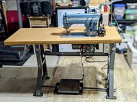 Full view of sewing machine mounted on wooden table and metal stand with foot pedal