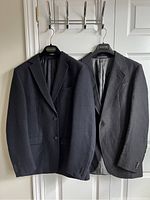 Two men's tailored jackets hanging side by side, dark colors, displaying front views and general style.