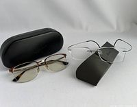 Two eyeglass frames side by side, Rayban semi-rimmed brown and gold frame with case to left and Silhouette rimless titanium frame on right with case.