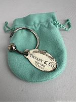 Tiffany & Co. silver keyring resting on a Tiffany blue pouch. Visible oval tag with hallmark and screwball detail missing.