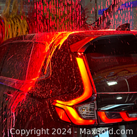 Photo showing a car undergoing a Lava Shine car wash with foam and water sprays illuminated by red light.