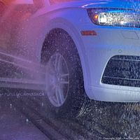 Photo showing a white vehicle being washed with water jets in the car wash facility.