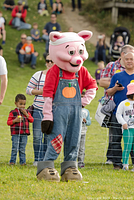 Person dressed in a pig mascot costume for Brooks Farms Fun Fall Festival standing in a field with spectators in the background