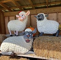 Three sheep sculptures displayed on hay bales inside a wooden shelter, representing part of the festival theme.