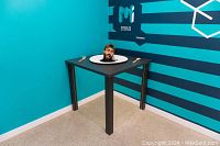 Illusion exhibit showing a person with their head appearing on a dining table using a perspective trick.