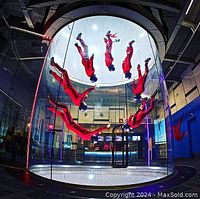 Indoor skydiving tunnel with multiple flyers in red suits inside the vertical wind tunnel at iFly, showing the flying experience and environment.