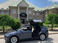 Grey Tesla Model X parked in front of a large winery building with one falcon-wing door open