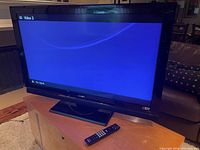 Sony 40-inch Bravia LCD TV powered on displaying "No signal" on input Video 2 and remote control on wooden surface.