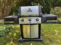 Front angled photo showing Broil King natural gas BBQ grill with 2 collapsible side shelves, control knobs and wheels.
