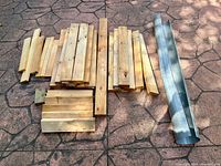 Photo showing assortment of construction lumber pieces approximately 4 inches wide and various lengths alongside a curved aluminum scrap piece.