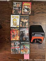 Photo showing 9 DVDs including The Bourne Supremacy, Kung Fu Panda, The Simpsons Movie, The Da Vinci Code, I Spy, King Kong, Tom Cruise Mission Impossible III, Russell Peters Comedy, and a zippered case.