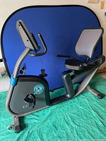 Side view of recumbent bike showing frame, pedals, and mesh-backed seat against blue background