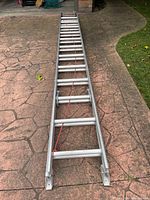 Top view of aluminum extension ladder laid on the ground, showing rungs and rope pulley system