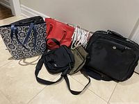 Photo showing 8 bags arranged on floor including a floral patterned tote, red structured handbag, several small crossbody bags, and a large black Dell computer bag