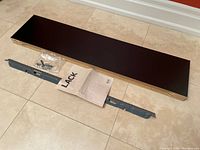 IKEA LACK shelf laid flat showing top surface, mounting bracket, screws in a small plastic bag, and instruction manual