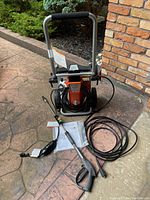 Full front view of power washer on wheeled frame with spray gun, lance, hose and manual laid out