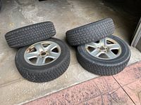 Four tires mounted on five-spoke alloy wheels arranged on garage floor.