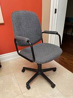 Front view of grey upholstered office chair with padded seat and back, black metal armrests, and black plastic five-wheel caster base.