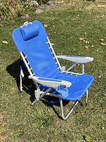 Blue beach chair on grass showing front side with headrest pillow and armrests