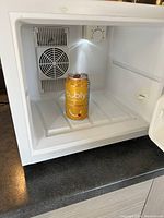 Photo showing inside the mini fridge with a can for size reference, displaying the cooling fan and temperature dial.