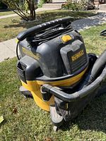 Front and side angle of yellow and black DeWalt wet/dry shop vacuum showing handle, hose with attachments, power cord wound on top.