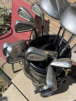 Close up view of irons and some drivers in the golf bag, showing club heads and model branding.