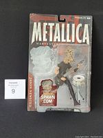 Full front view of the Metallica Jason Newsted figurine in sealed packaging showing figurine, bass guitar and drum stand accessory inside.