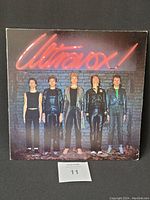 Front cover of Ultravox vinyl record showing five band members in black leather outfits standing against a brick wall with the Ultravoid logo in neon orange at top.
