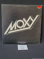 Front cover of Moxy vinyl album showing black background with large silver 3D band name logo.