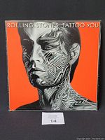 Front cover of the Rolling Stones Tattoo You album vinyl record showing a stylized black and white portrait on an orange background.
