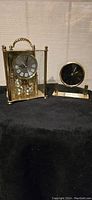 Gold-tone rectangular clock and smaller round black dial clock side by side on black cloth.