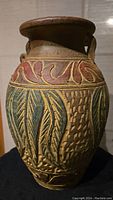Front view of clay vase showing top and carved painted patterns in red and green with visible handle damage.