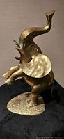 Side view of brass elephant statue showing raised trunk, extended ears, and detailed features on textured oval base.