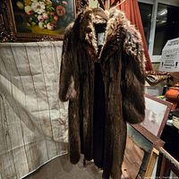 Front view of the long brown natural fur coat with full collar and three-quarter sleeves displayed on a hanger indoors.